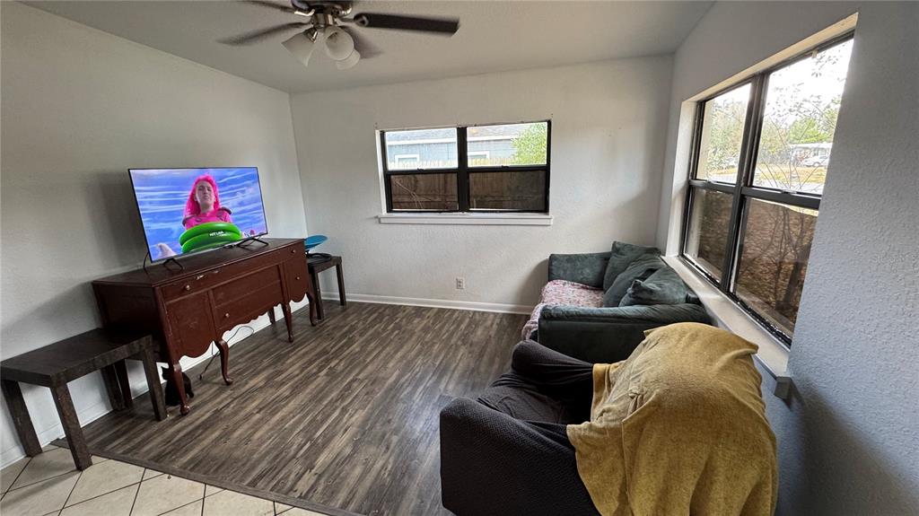 A living room features wood-look flooring, a ceiling fan, a television on a sideboard, and furniture — 2925 BELLWOOD AVENUE, LAKELAND, FL