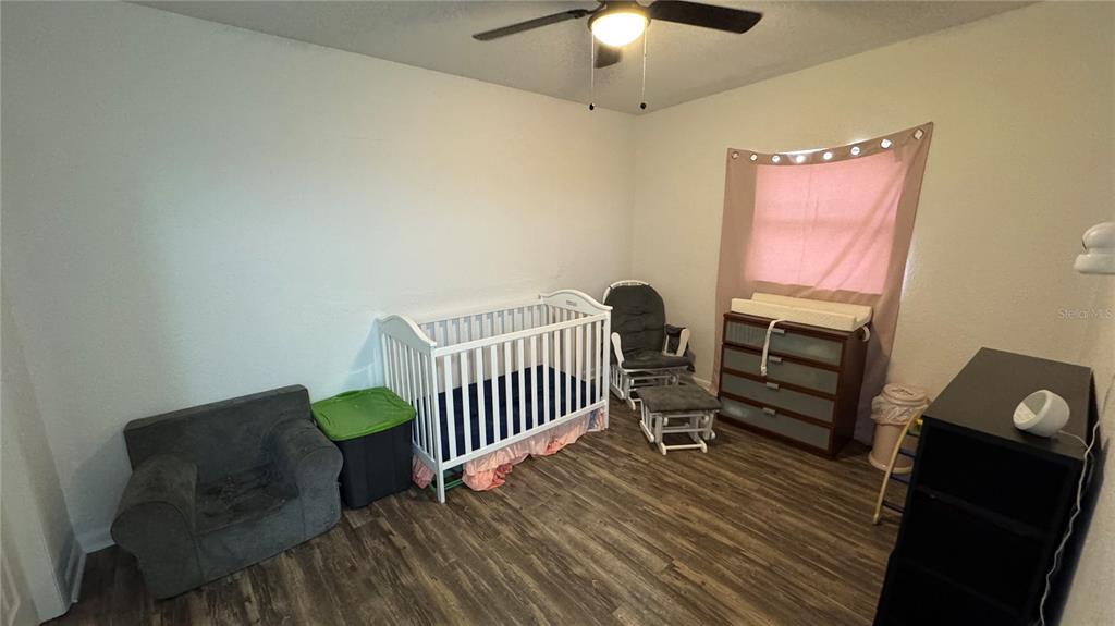 A nursery features a white crib, a rocking chair, a dresser, and wood-look flooring — 2925 BELLWOOD AVENUE, LAKELAND, FL