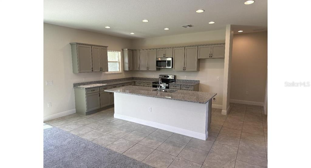 A kitchen features gray cabinets, granite countertops, a central island, and tile flooring — 2573 TULSA AVENUE, NORTH PORT, FL