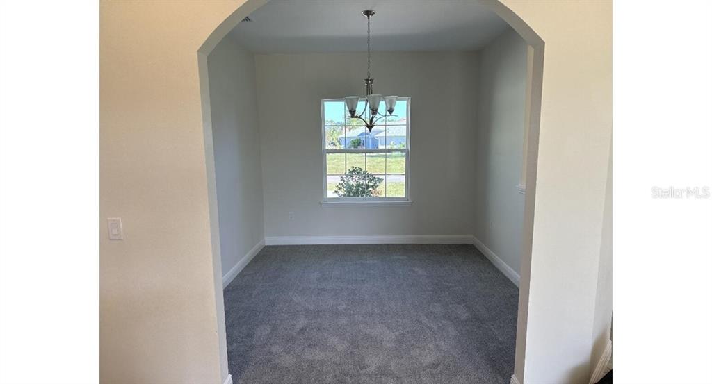 A carpeted dining room features an arched entryway, a single window, and a hanging chandelier — 2573 TULSA AVENUE, NORTH PORT, FL