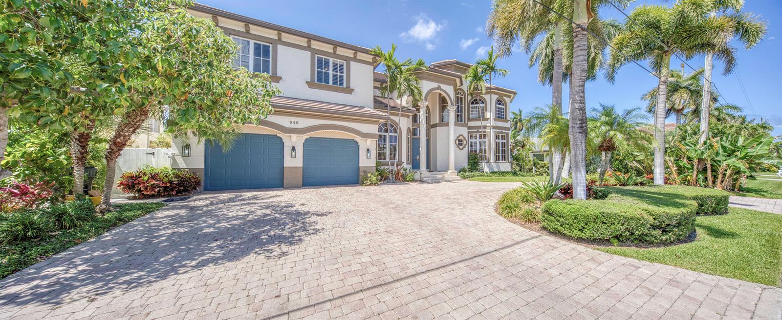 A two-story house with a paved driveway, blue garage doors, and palm trees — 945 Cypress Drive, Delray Beach FL 33483, DELRAY BEACH, FL