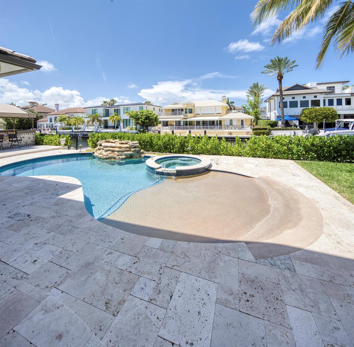A backyard swimming pool features a rock waterfall, a built-in spa, and a tanning ledge — 945 Cypress Drive, Delray Beach FL 33483, DELRAY BEACH, FL
