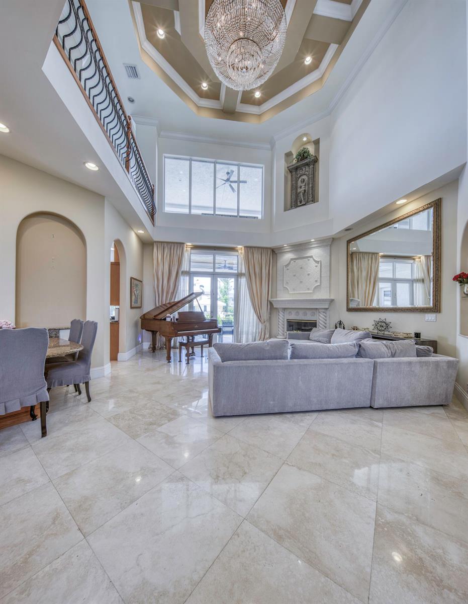 A spacious living room features a grand piano, a fireplace, and a large crystal chandelier — 945 Cypress Drive, Delray Beach FL 33483, DELRAY BEACH, FL
