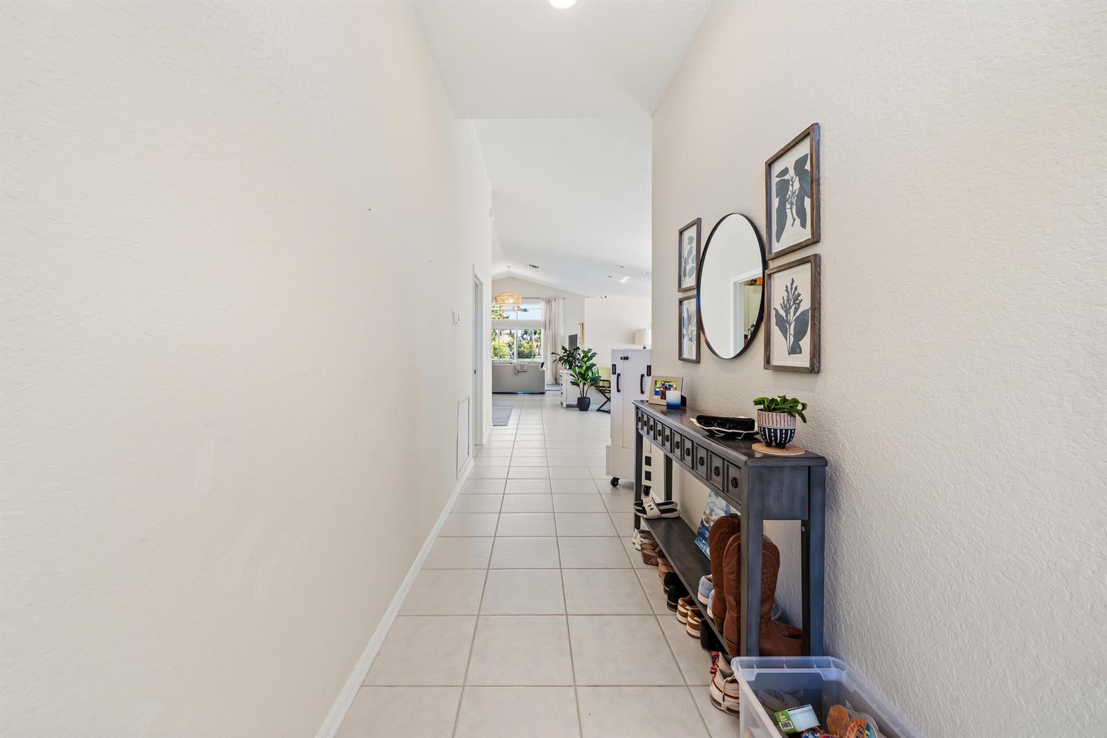 A hallway with light tile flooring leads toward an open living area with a console table — 3817 Miramontes Circle, Wellington FL 33414, WELLINGTON, FL