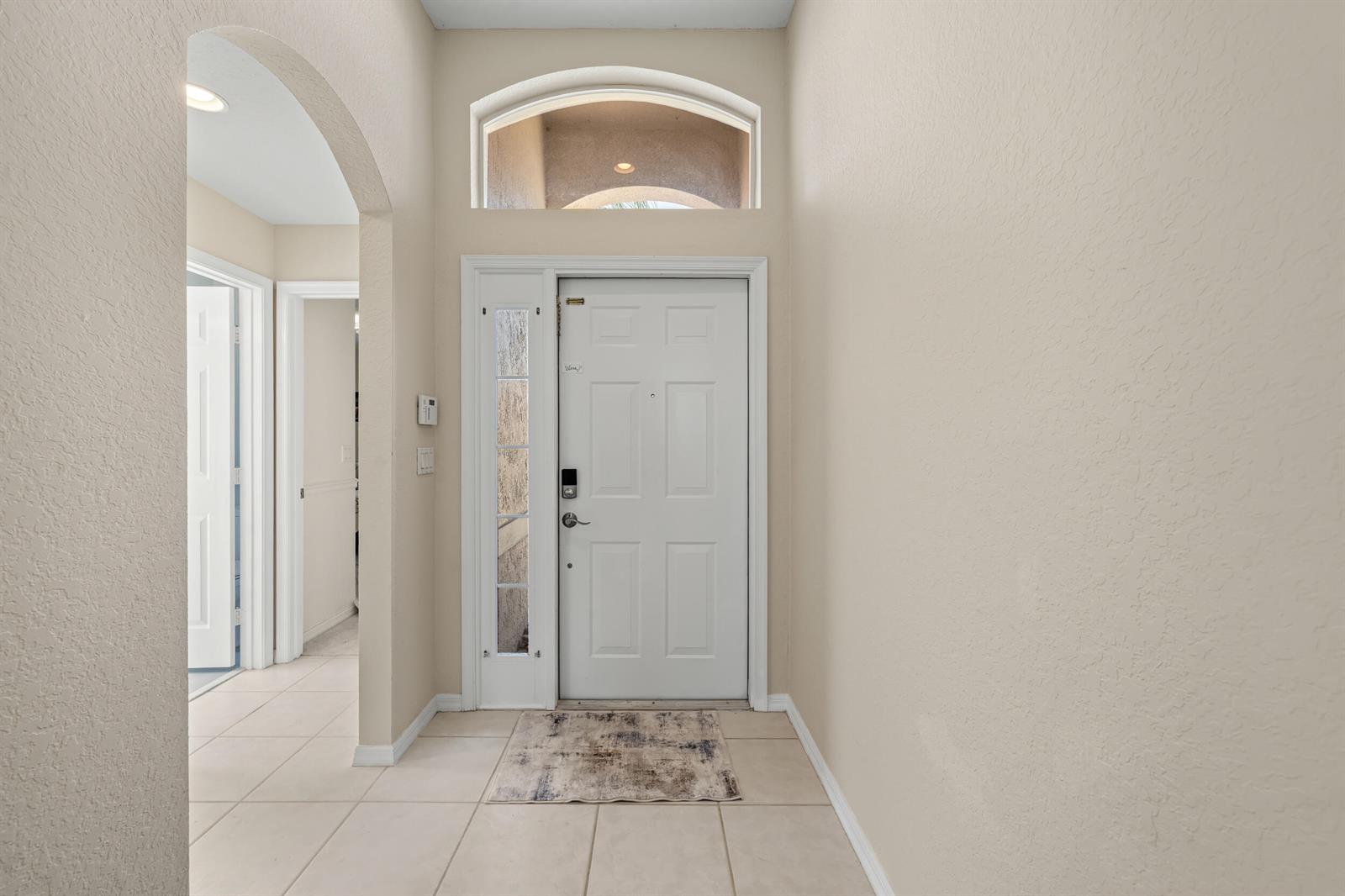 An entryway features a white front door with a sidelight, arched transom window, and tile flooring — 3817 Miramontes Circle, Wellington FL 33414, WELLINGTON, FL