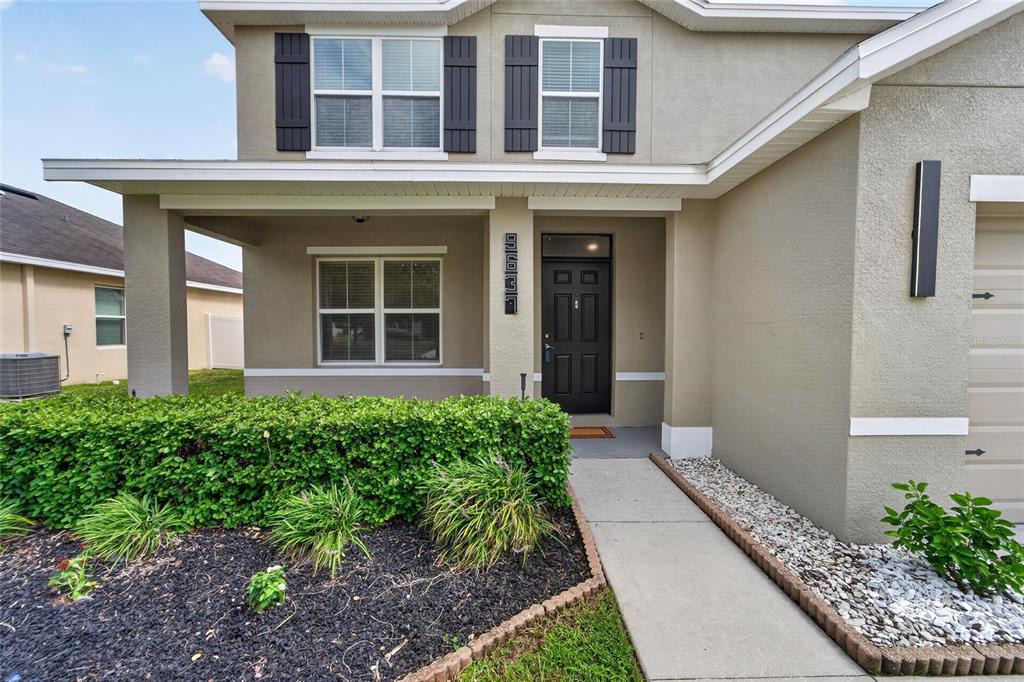 The exterior of a two-story house features a covered porch, a front door, and landscaping — 9637 TRONCAIS CIRCLE, THONOTOSASSA, FL