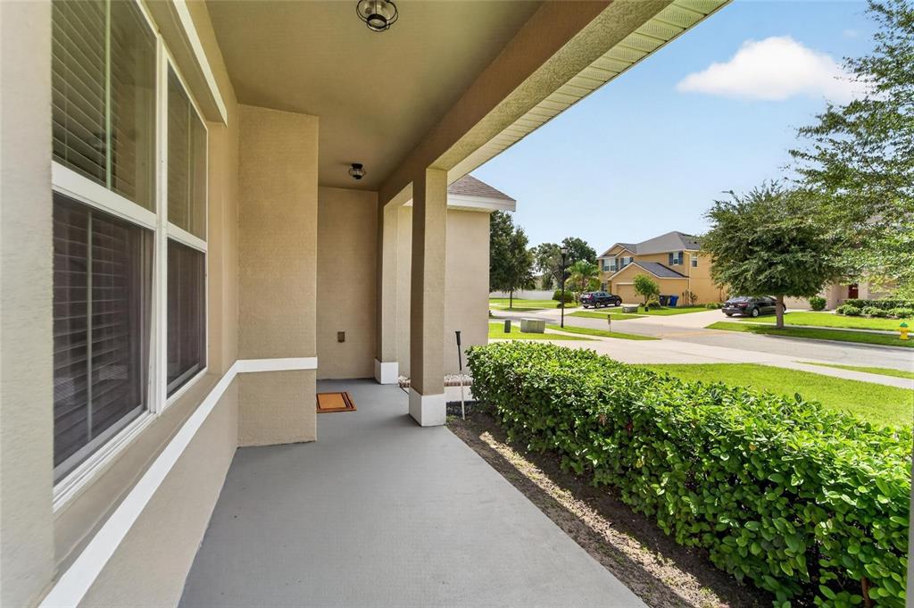 A covered concrete porch overlooks a suburban street with a green hedge and trees — 9637 TRONCAIS CIRCLE, THONOTOSASSA, FL