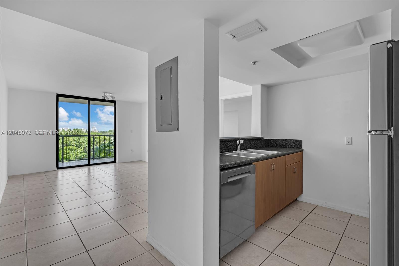 A kitchen with wood cabinets and a dishwasher opens to a tiled living area — 1690 SW 27th Ave # 608, Miami FL 33145, MIAMI, FL