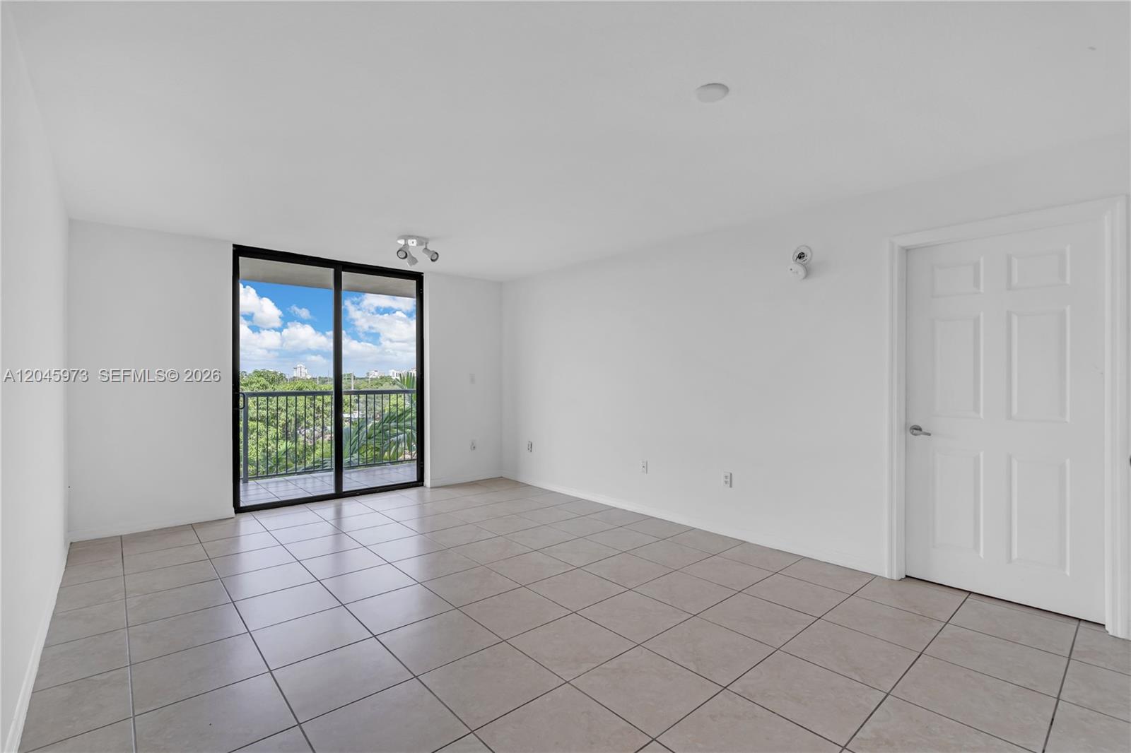 An empty room features white walls, light-colored tile flooring, a sliding glass door, and balcony — 1690 SW 27th Ave # 608, Miami FL 33145, MIAMI, FL