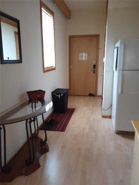 An entryway with light wood flooring, a glass-topped console table, and a white refrigerator — 101 PALM HARBOR PARKWAY UNIT C226, PALM COAST, FL