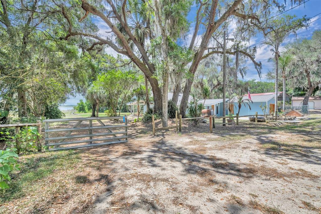 A metal gate stands at the entrance of a dirt driveway leading toward a house — 13450 SE 105TH TERRACE, OCKLAWAHA, FL