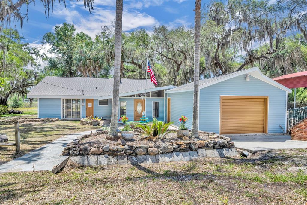A light blue house with a garage, stone landscaping, and a flag in the front yard — 13450 SE 105TH TERRACE, OCKLAWAHA, FL