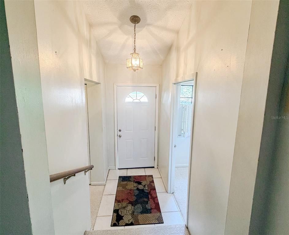 A tiled entryway features a white front door, a hanging light fixture, and carpeted stairs — 5616 SILVER SANDS CIRCLE, KEYSTONE HEIGHTS, FL
