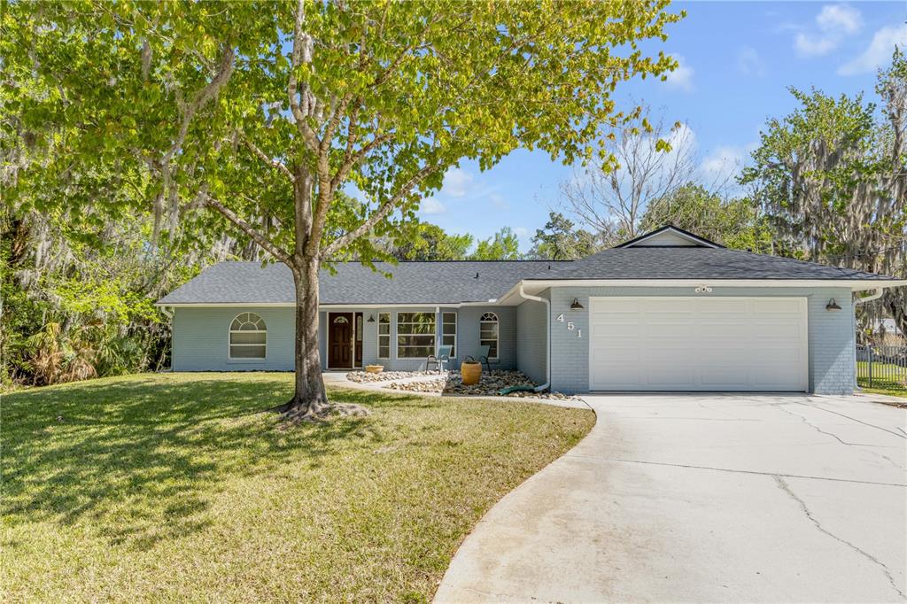 A single-story house with a light blue brick exterior, a two-car garage, and a large tree — 451 PALM DRIVE, NEW SMYRNA BEACH, FL