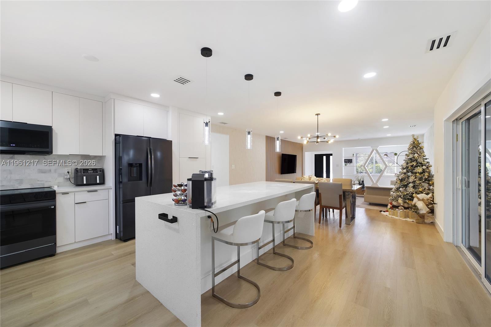 A modern open-concept kitchen features white cabinetry, a large quartz island, and light wood flooring — 45 NE 124th Ter, North Miami FL 33161, NORTH MIAMI, FL