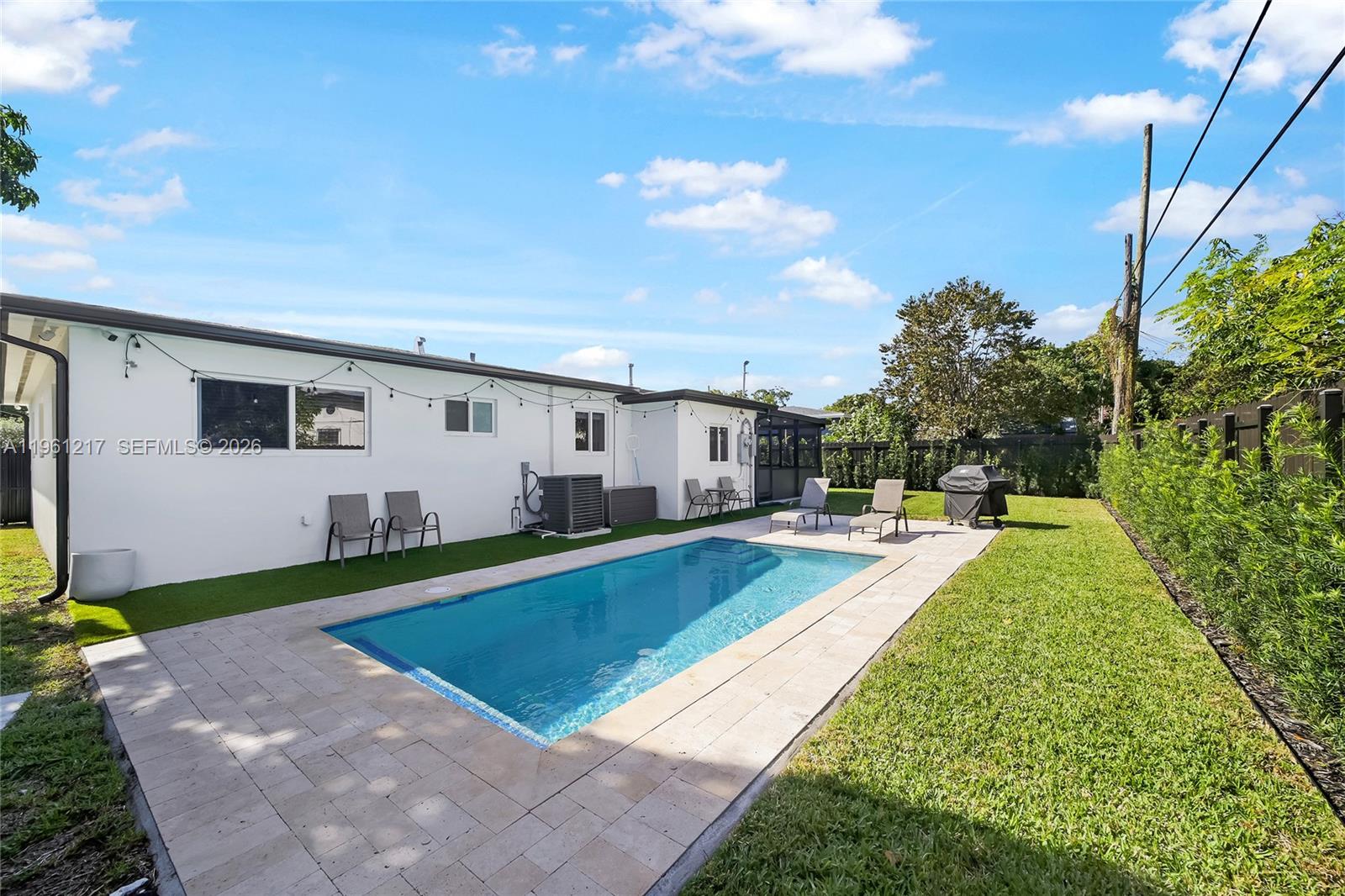 A backyard features a rectangular swimming pool, stone patio, artificial turf, and a white house — 45 NE 124th Ter, North Miami FL 33161, NORTH MIAMI, FL