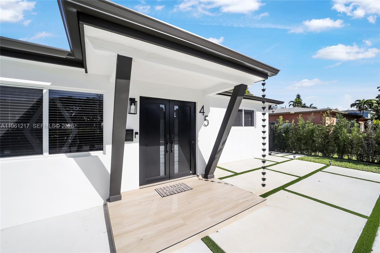 The exterior of a modern home features a covered entryway with double doors and concrete pavers — 45 NE 124th Ter, North Miami FL 33161, NORTH MIAMI, FL