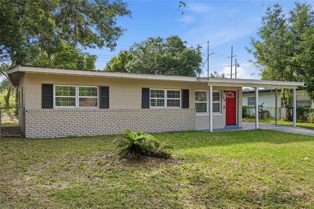 A single-story house with a beige exterior, brick base, black shutters, and a red door — 224 MURRY DRIVE, ORLANDO, FL