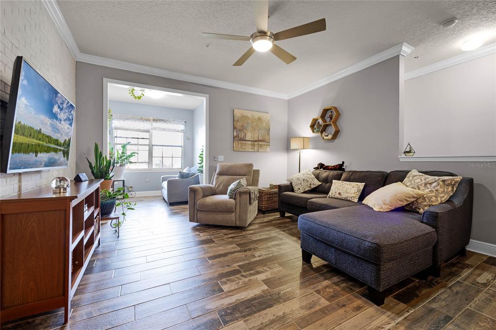 A living room features wood-look tile flooring, a gray sectional sofa, and a ceiling fan — 430 SOUTHERN PECAN CIRCLE UNIT 207, WINTER GARDEN, FL