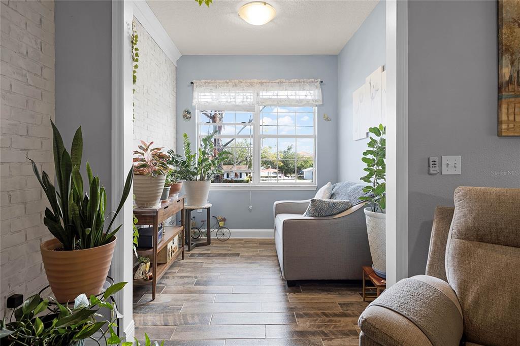 A sunroom features a white brick wall, wood-look tile flooring, and a window view — 430 SOUTHERN PECAN CIRCLE UNIT 207, WINTER GARDEN, FL
