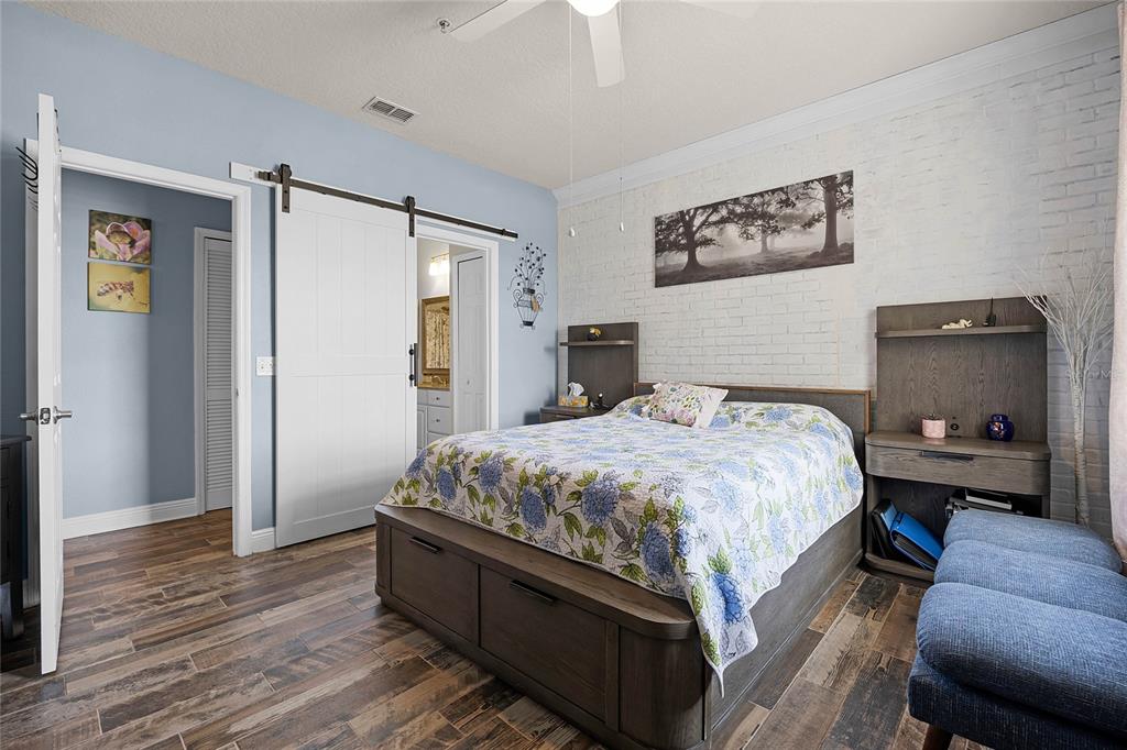 A bedroom with a white brick accent wall, wood-look tile flooring, and a sliding barn door — 430 SOUTHERN PECAN CIRCLE UNIT 207, WINTER GARDEN, FL