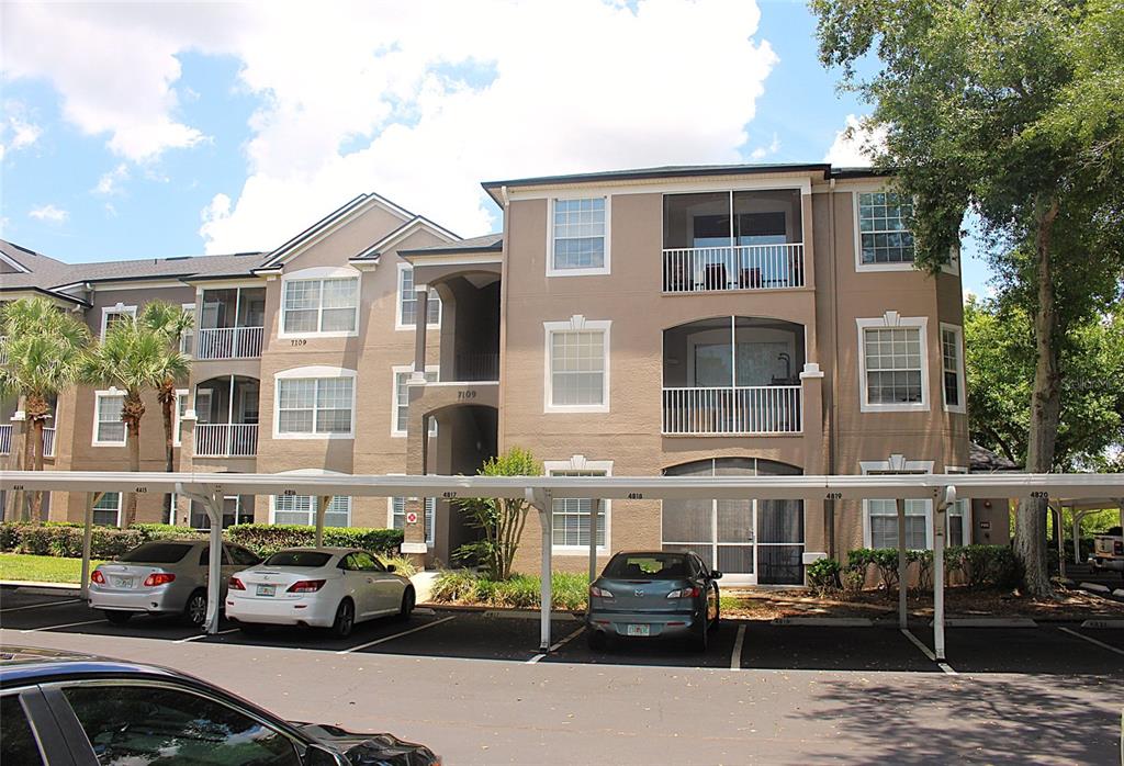 A multi-story apartment building with a parking carport in the foreground — 7109 YACHT BASIN AVENUE UNIT 428, ORLANDO, FL