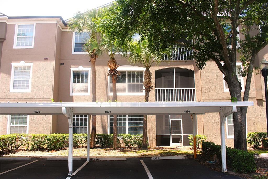 An exterior view of a multi-story apartment building with a covered parking structure in front — 7109 YACHT BASIN AVENUE UNIT 428, ORLANDO, FL