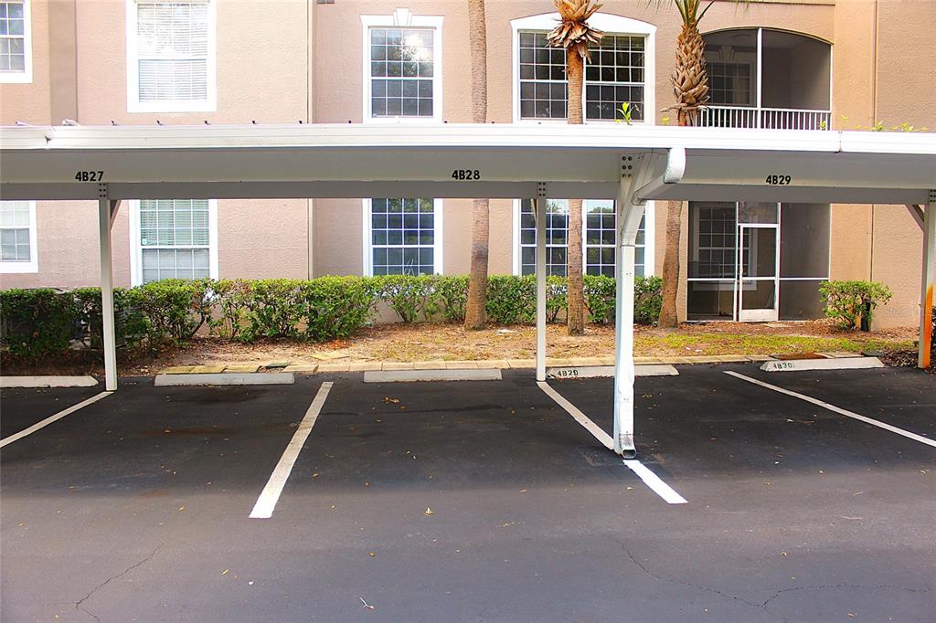 A covered parking area with numbered spaces sits in front of a multi-story apartment building — 7109 YACHT BASIN AVENUE UNIT 428, ORLANDO, FL