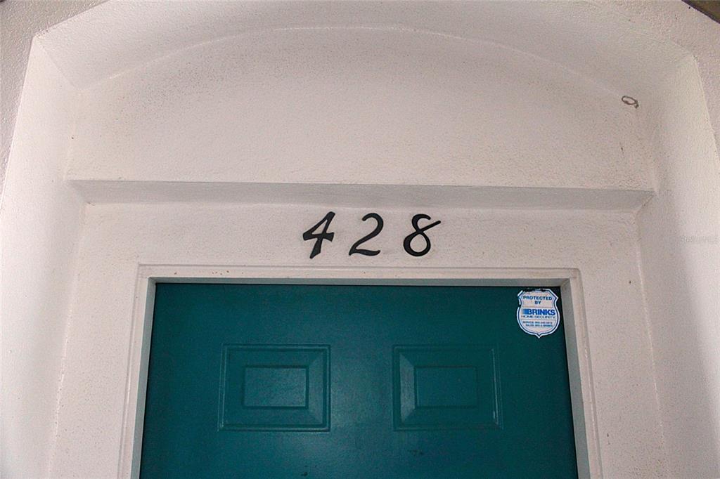 A teal front door with the number 428 above it and a security system sticker — 7109 YACHT BASIN AVENUE UNIT 428, ORLANDO, FL
