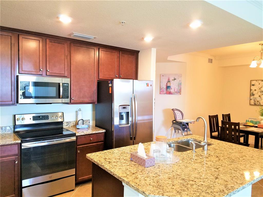A kitchen features dark wood cabinets, granite countertops, stainless steel appliances, and a central island — 17108 VARDON TERRACE UNIT 208, LAKEWOOD RANCH, FL