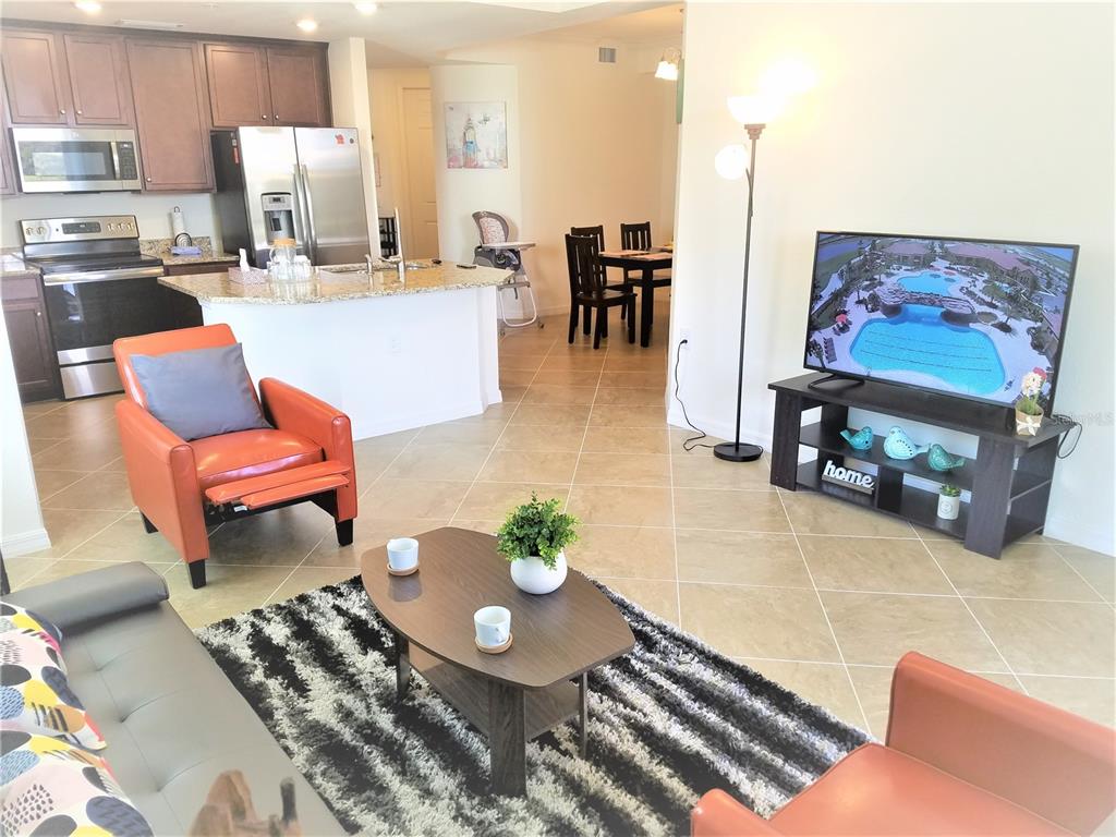 An open-concept living room and kitchen area featuring tile flooring, a television, and furniture — 17108 VARDON TERRACE UNIT 208, LAKEWOOD RANCH, FL