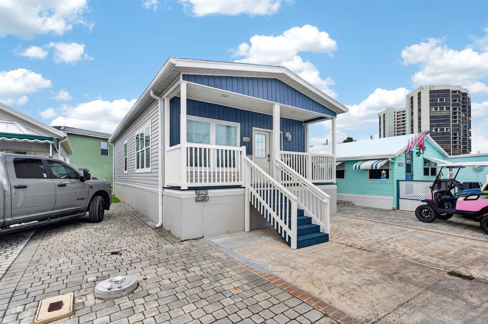 A blue manufactured home with a front porch and stairs sits on a paved lot — 2149 Nettles Boulevard, Jensen Beach FL 34957, JENSEN BEACH, FL