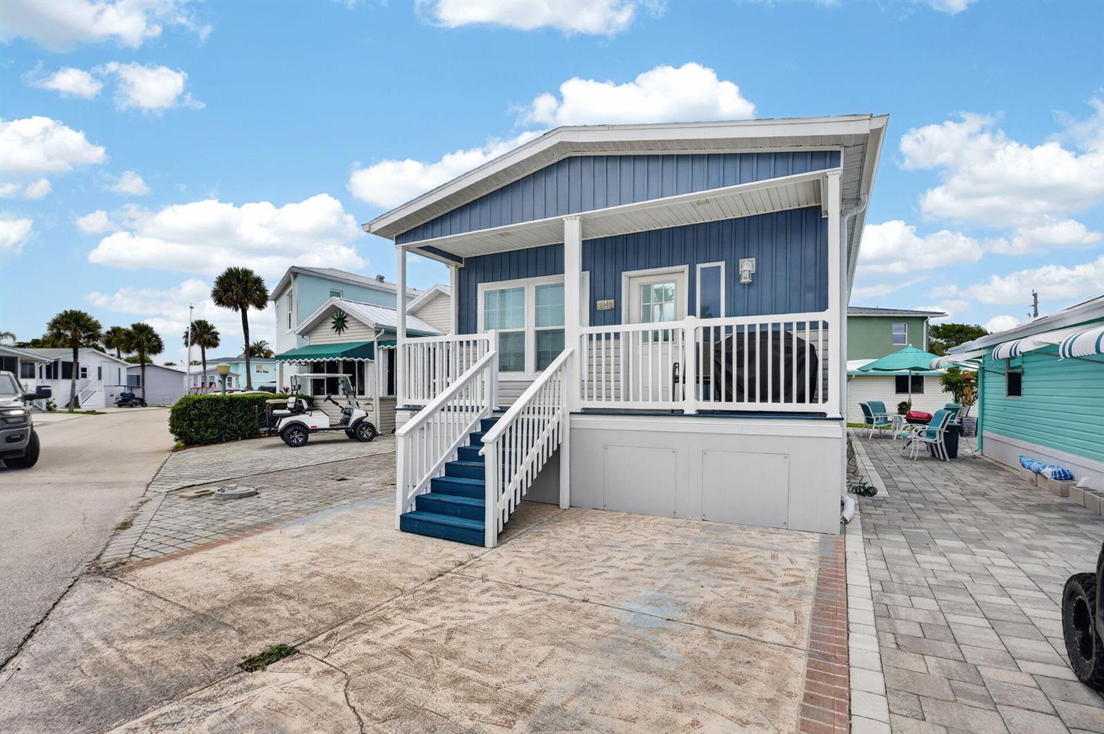 A blue mobile home features a white porch with stairs and a paved driveway — 2149 Nettles Boulevard, Jensen Beach FL 34957, JENSEN BEACH, FL