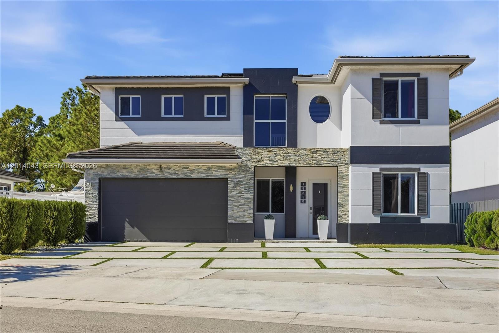 A two-story house features a stone facade, a dark garage door, and a paved driveway — 18350 SW 139th Path, Miami FL 33177, MIAMI, FL