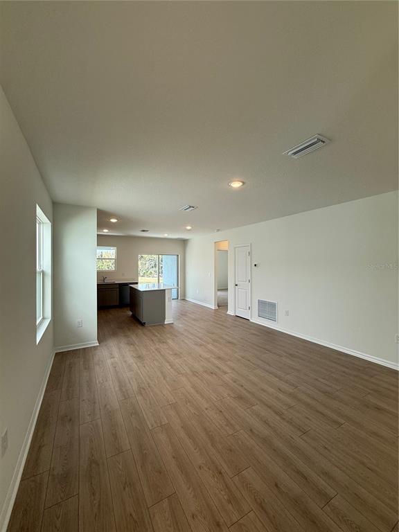 An open-concept living area with light wood-look flooring, a kitchen island, and white walls — 13044 SASSAFRAS TRAIL, PARRISH, FL