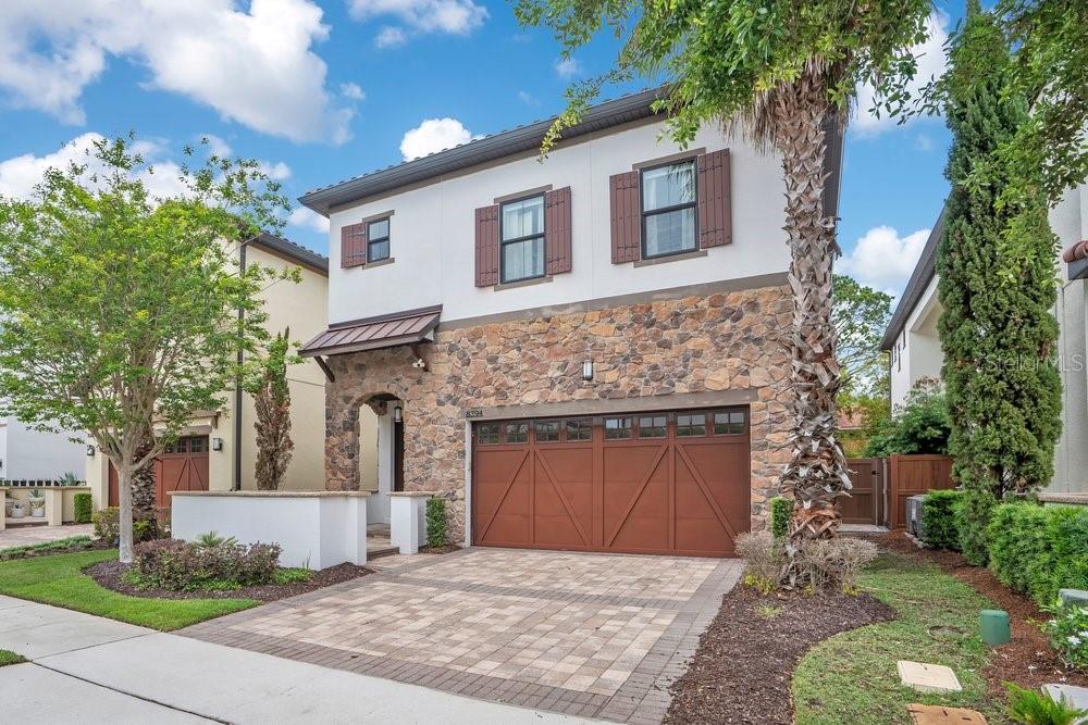 A two-story house with a stone facade, brown garage door, and brown window shutters — 8394 VIA VITTORIA WAY, ORLANDO, FL