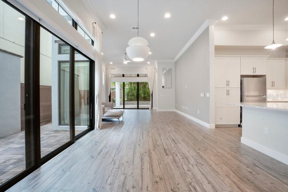 A bright living area with wood-look flooring, white cabinetry, and large sliding glass doors — 8394 VIA VITTORIA WAY, ORLANDO, FL