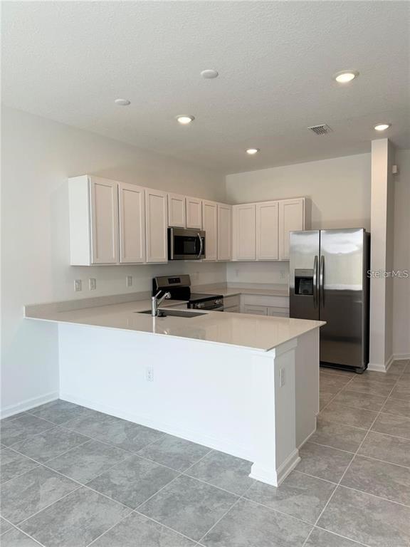 A kitchen features white cabinets, stainless steel appliances, and a peninsula with quartz countertops — 2452 SKYLINE LOOP, KISSIMMEE, FL