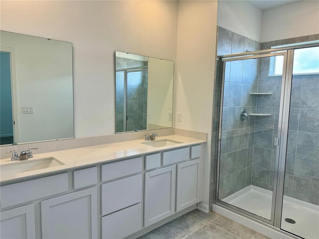 A bathroom features a double vanity with white cabinets, quartz countertops, and a glass shower — 2452 SKYLINE LOOP, KISSIMMEE, FL