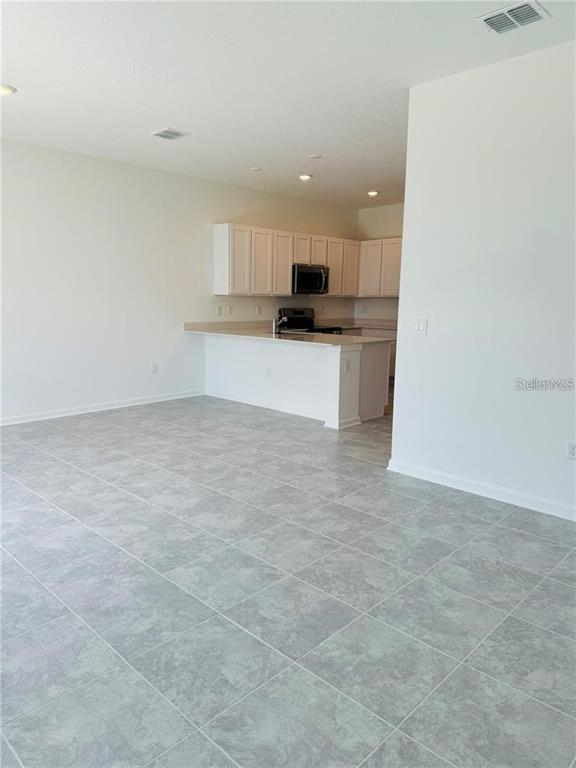 A kitchen with white cabinets and a breakfast bar overlooks a tiled living area — 2452 SKYLINE LOOP, KISSIMMEE, FL