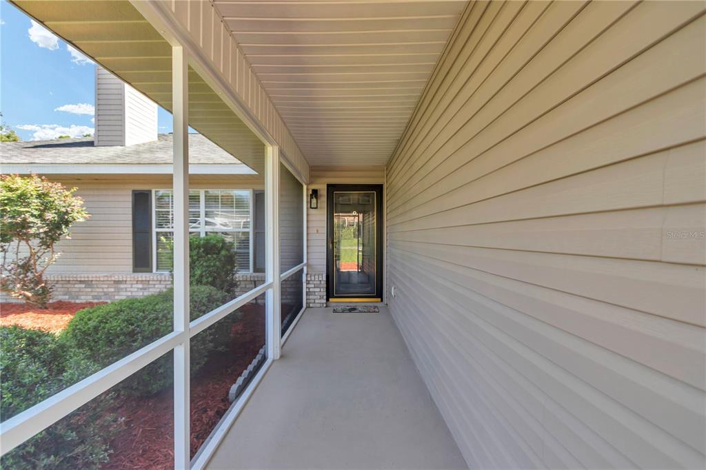 A covered entryway features light-colored horizontal siding, a concrete floor, and a glass-paneled front door — 63 PECAN PASS, OCALA, FL