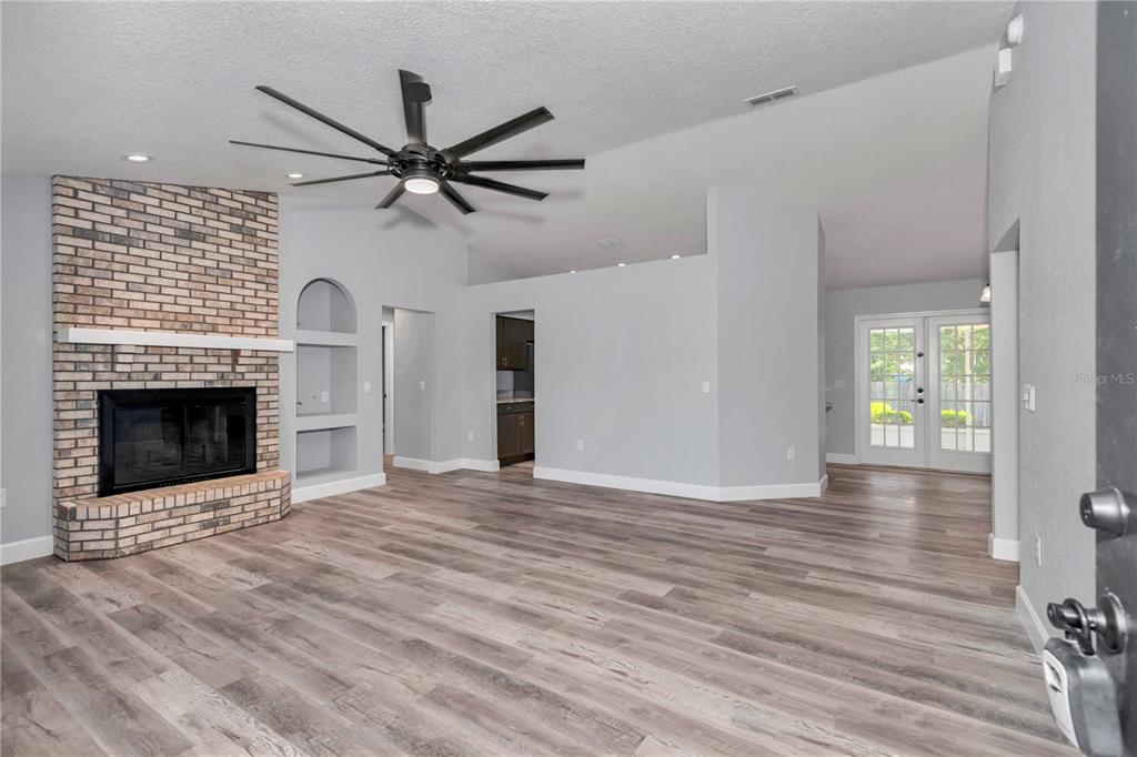 A living room with a brick fireplace, wood-look flooring, and a ceiling fan — 63 PECAN PASS, OCALA, FL