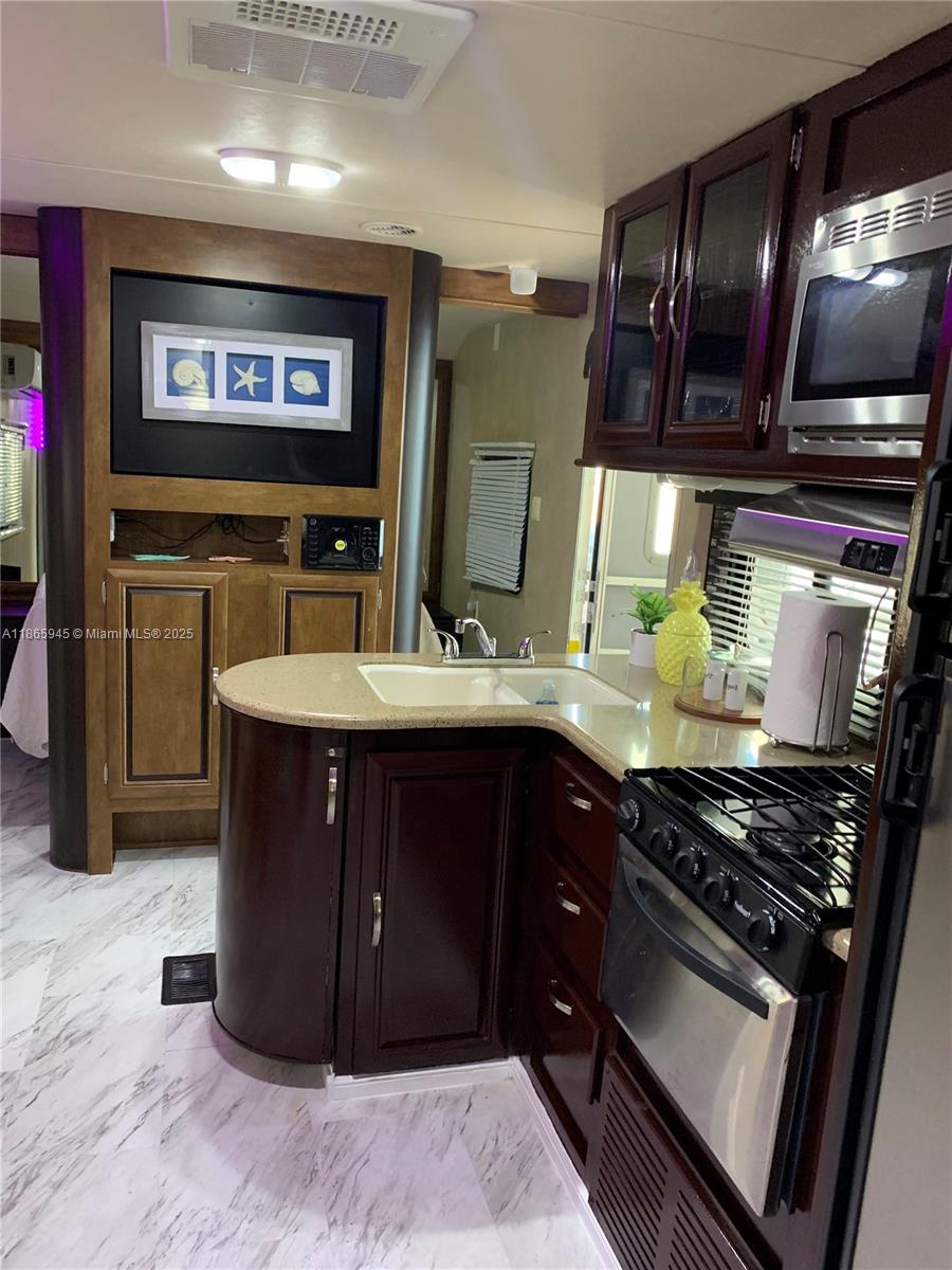A kitchen with dark wood cabinets, a gas stove, and a double sink in an RV — 325 Calusa St #120, Key Largo FL 33037, KEY LARGO, FL