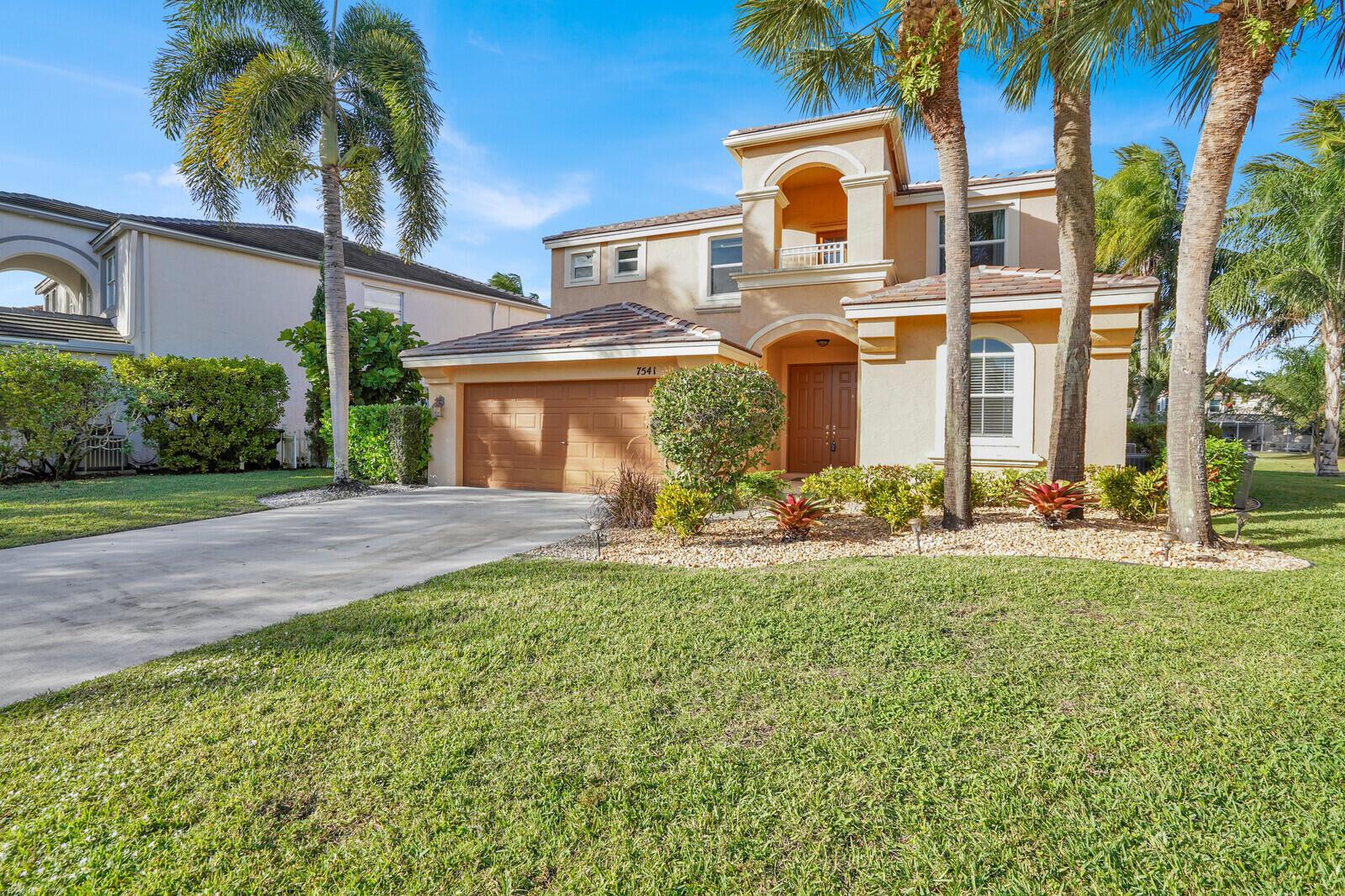 A two-story tan stucco house with a tile roof, garage, and palm trees in front — 7541 Downwinds Lane, Lake Worth FL 33467, LAKE WORTH, FL