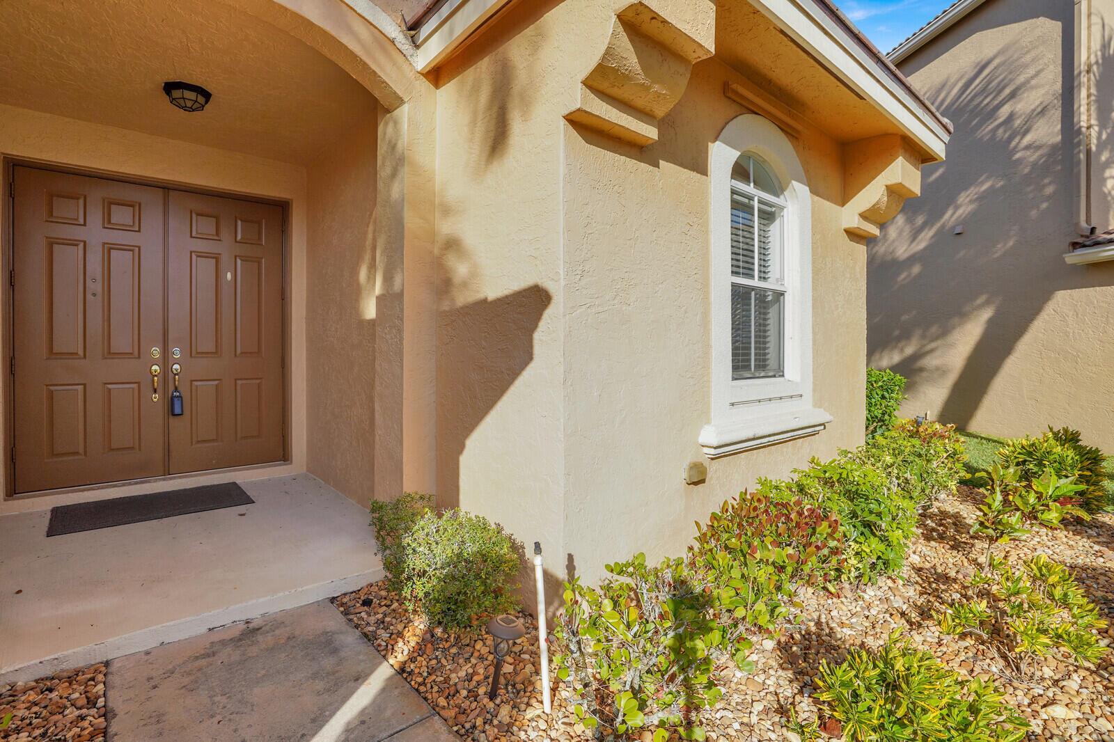 A tan stucco house exterior features a double front door and a single arched window — 7541 Downwinds Lane, Lake Worth FL 33467, LAKE WORTH, FL
