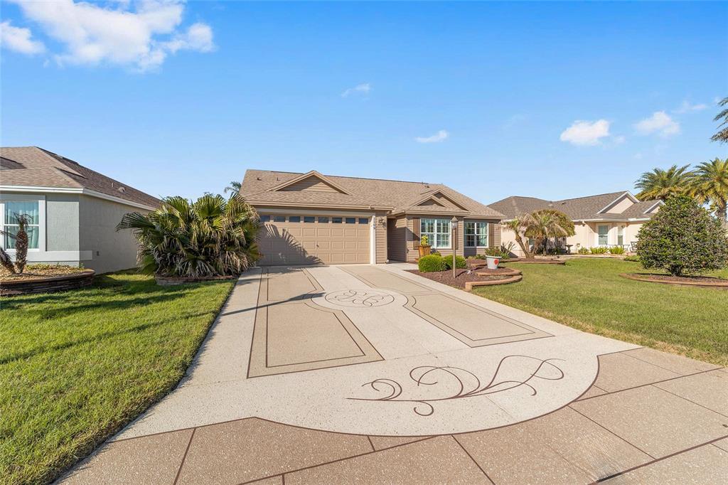 A single-story suburban house with a tan exterior, two-car garage, and a gravel front yard — 1109 ALCOVE LOOP, THE VILLAGES, FL