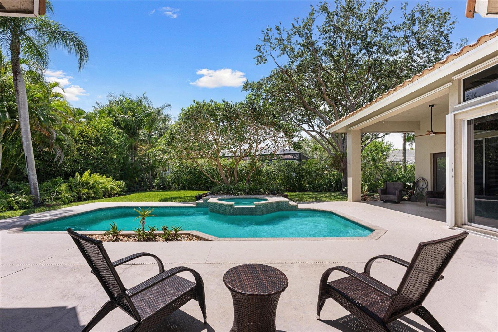 A backyard patio features a swimming pool with a spa, lounge chairs, and lush landscaping — 10331 NW 62nd Drive, Parkland FL 33076, PARKLAND, FL