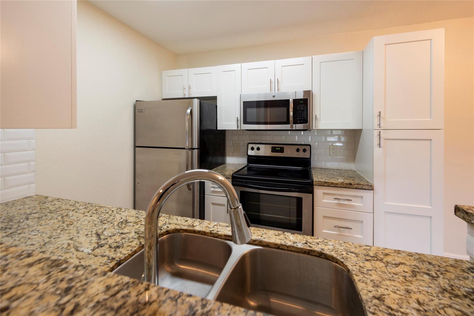 A kitchen features stainless steel appliances, white cabinets, and granite countertops with a double sink — 2906 S University Drive # 10104, Davie FL 33328, DAVIE, FL