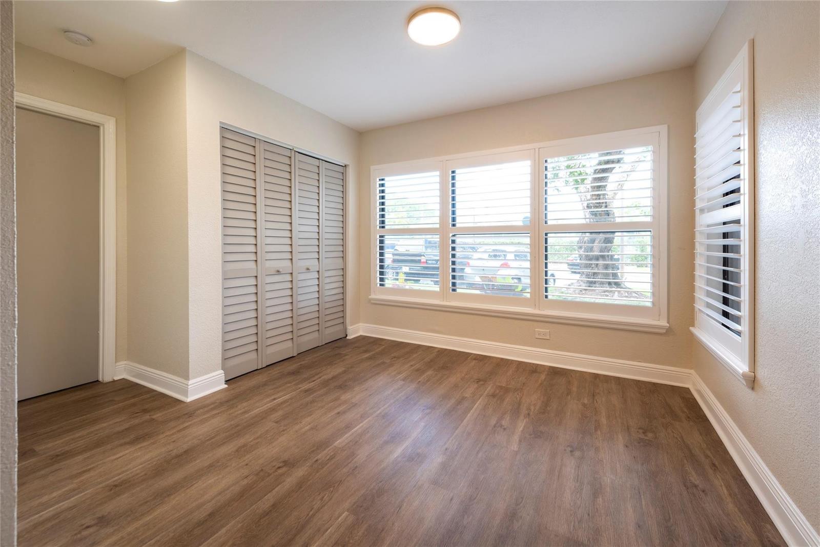 An empty bedroom features wood-look flooring, louvered closet doors, and windows with white plantation shutters — 2906 S University Drive # 10104, Davie FL 33328, DAVIE, FL