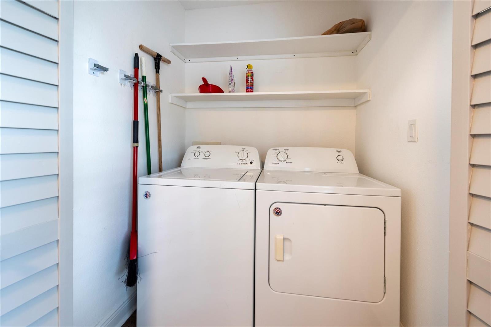 A laundry closet features a white washer and dryer, two wall-mounted shelves, and cleaning tools — 2906 S University Drive # 10104, Davie FL 33328, DAVIE, FL